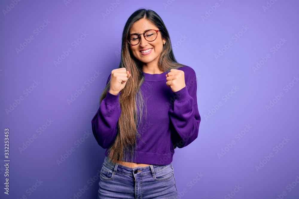 Young beautiful smart woman wearing glasses over purple isolated background excited for success with arms raised and eyes closed celebrating victory smiling. Winner concept. Young beautiful smart woman wearing glasses over purple isolated background excited for success with arms raised and eyes closed celebrating victory smiling. Winner concept.