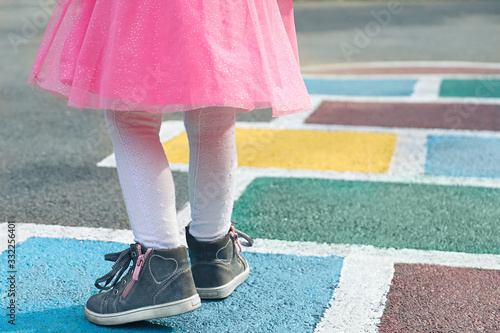 Closeup of girl s legs in a pink dress and hopscotch drawn on asphalt. Child playing hopscotch on playground outdoors on a sunny day. outdoor activities for children.