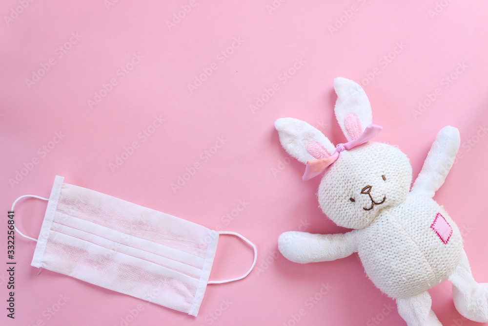Fototapeta premium White toy rabbit with white mask and gloves on isolated pink background. Happy easter concept with coronavirus risk. Canceled easter.