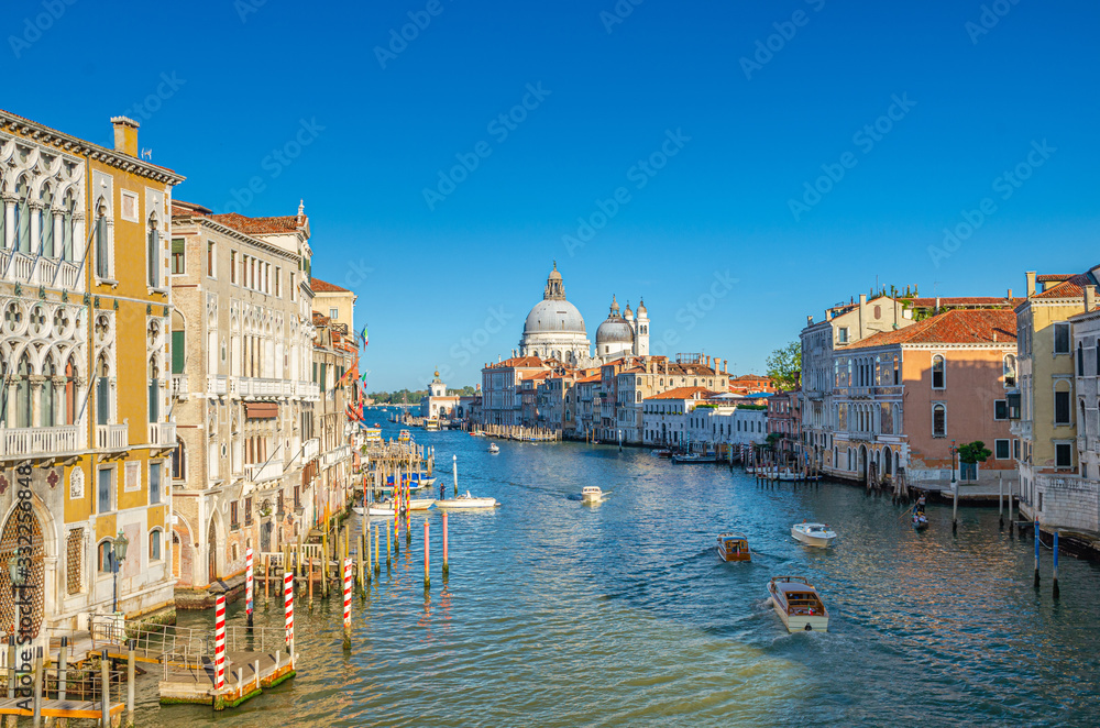 Venice cityscape with Grand Canal waterway. Gondolas, boats, vaporettos docked and sailing Canal Grande. Santa Maria della Salute Roman Catholic church on Punta della Dogana. Veneto Region, Italy.
