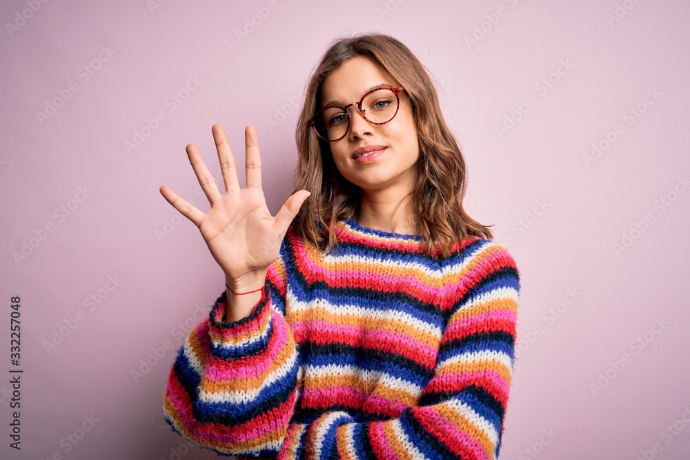 Young beautiful blonde girl wearing glasses and casual sweater over pink isolated background showing and pointing up with fingers number five while smiling confident and happy. Young beautiful blonde girl wearing glasses and casual sweater over pink isolated background showing and pointing up with fingers number five while smiling confident and happy.