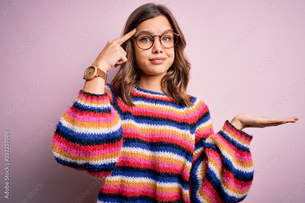 Young beautiful blonde girl wearing glasses and casual sweater over pink isolated background confused and annoyed with open palm showing copy space and pointing finger to forehead. Think about it. Young beautiful blonde girl wearing glasses and casual sweater over pink isolated background confused and annoyed with open palm showing copy space and pointing finger to forehead. Think about it.