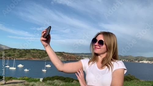Happy blonde woman tourist taking landscape photos of the sea from hill top