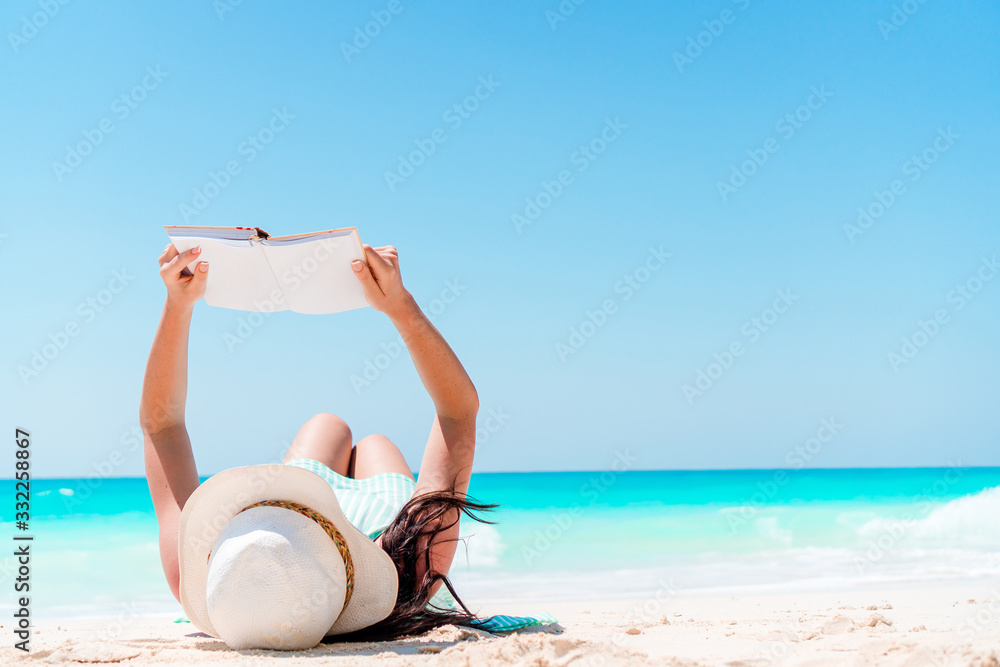Fototapeta premium Young woman reading book during tropical white beach
