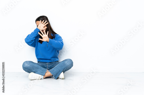 Young mixed race woman sitting on the floor isolated on white background nervous stretching hands to the front