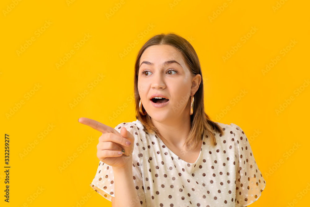 Beautiful young woman showing something on color background
