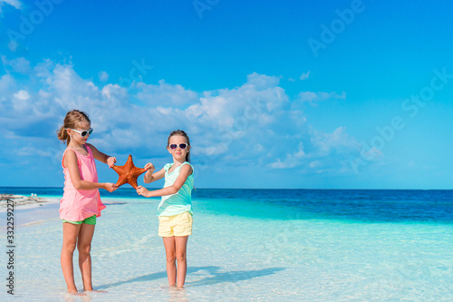 Adorable little girls with starfish on white empty beach