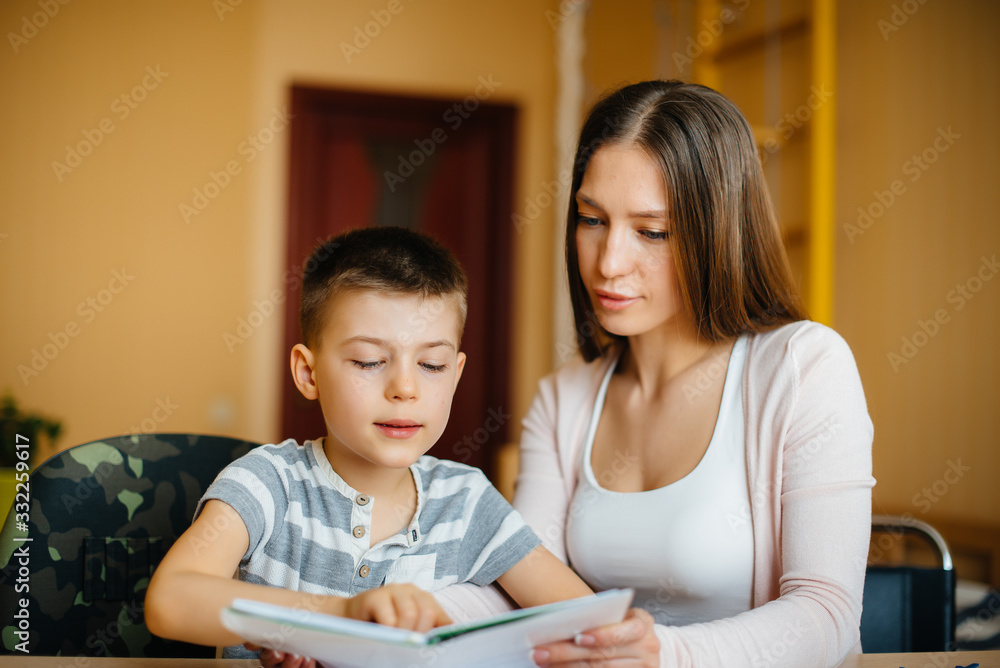 A young mother is doing homework with her son at home. Parents and training A young mother is doing homework with her son at home. Parents and training
