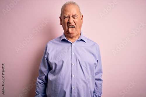 Middle age handsome hoary man wearing casual shirt standing over pink background sticking tongue out happy with funny expression. Emotion concept.