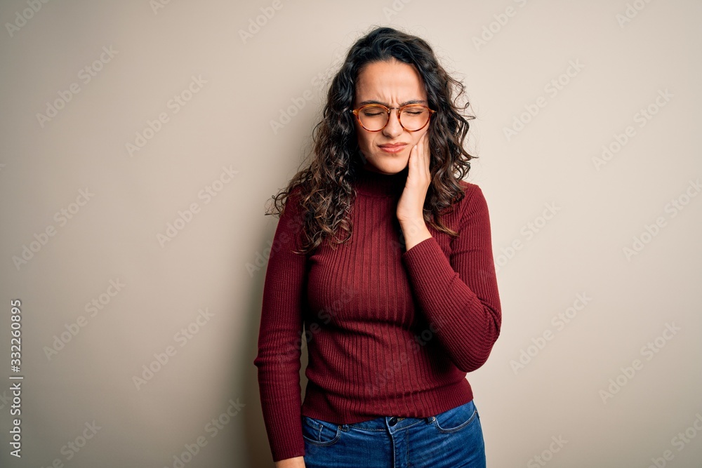 Beautiful woman with curly hair wearing casual sweater and glasses over white background touching mouth with hand with painful expression because of toothache or dental illness on teeth. Dentist Beautiful woman with curly hair wearing casual sweater and glasses over white background touching mouth with hand with painful expression because of toothache or dental illness on teeth. Dentist
