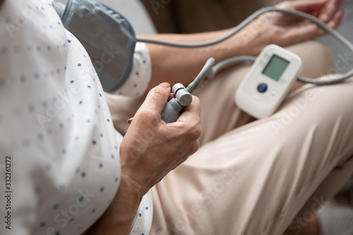 Close up older woman using semi-automatic digital tonometer, measuring blood pressure herself at home. Elder retired lady suffering from hypertension, controlling health condition, disease prevention.