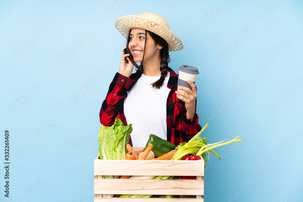 Young farmer Woman holding fresh vegetables in a wooden basket holding coffee to take away and a mobile