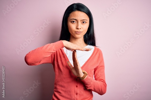 Young beautiful chinese woman wearing casual sweater over isolated pink background Doing time out gesture with hands, frustrated and serious face