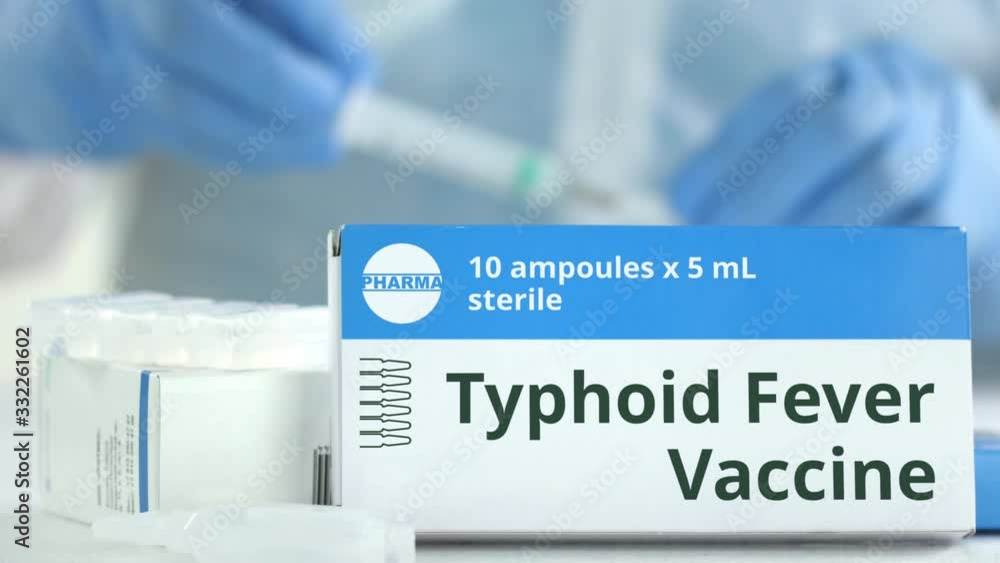Box with typhoid fever vaccine on the table against blurred lab assistant or doctor. Fictional phaceutical logo Box with typhoid fever vaccine on the table against blurred lab assistant or doctor. Fictional phaceutical logo