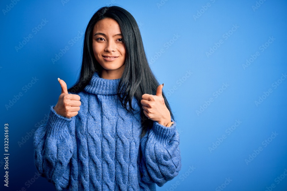 Young beautiful chinese woman wearing casual sweater over isolated blue background success sign doing positive gesture with hand, thumbs up smiling and happy. Cheerful expression and winner gesture. Young beautiful chinese woman wearing casual sweater over isolated blue background success sign doing positive gesture with hand, thumbs up smiling and happy. Cheerful expression and winner gesture.