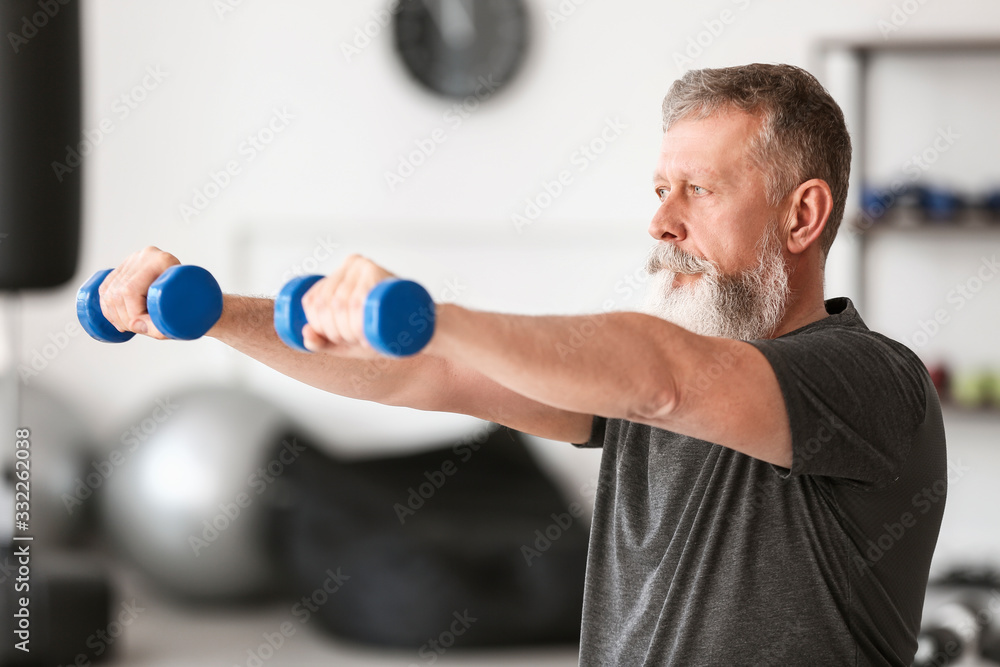 Sporty elderly man training with dumbbells in gym Sporty elderly man training with dumbbells in gym