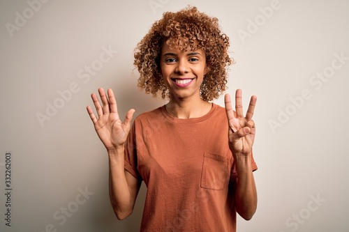 Beautiful african american woman with curly hair wearing casual t-shirt over white background showing and pointing up with fingers number eight while smiling confident and happy.