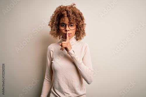 Young african american woman wearing turtleneck sweater and glasses over white background asking to be quiet with finger on lips. Silence and secret concept.
