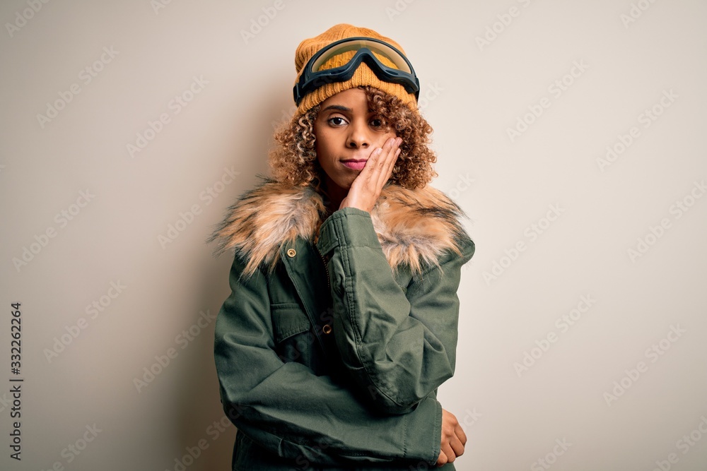 Young african american skier woman with curly hair wearing snow sportswear and ski goggles thinking looking tired and bored with depression problems with crossed arms.