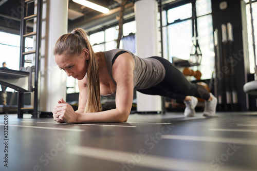 Full length portrait of sportive young woman doing plank exercise during strength workout in modern gym, copy space