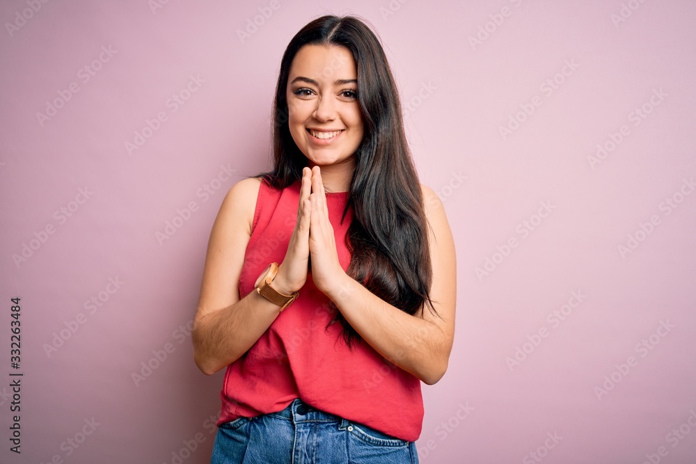 Young brunette woman wearing casual summer shirt over pink isolated background praying with hands together asking for forgiveness smiling confident. Young brunette woman wearing casual summer shirt over pink isolated background praying with hands together asking for forgiveness smiling confident.