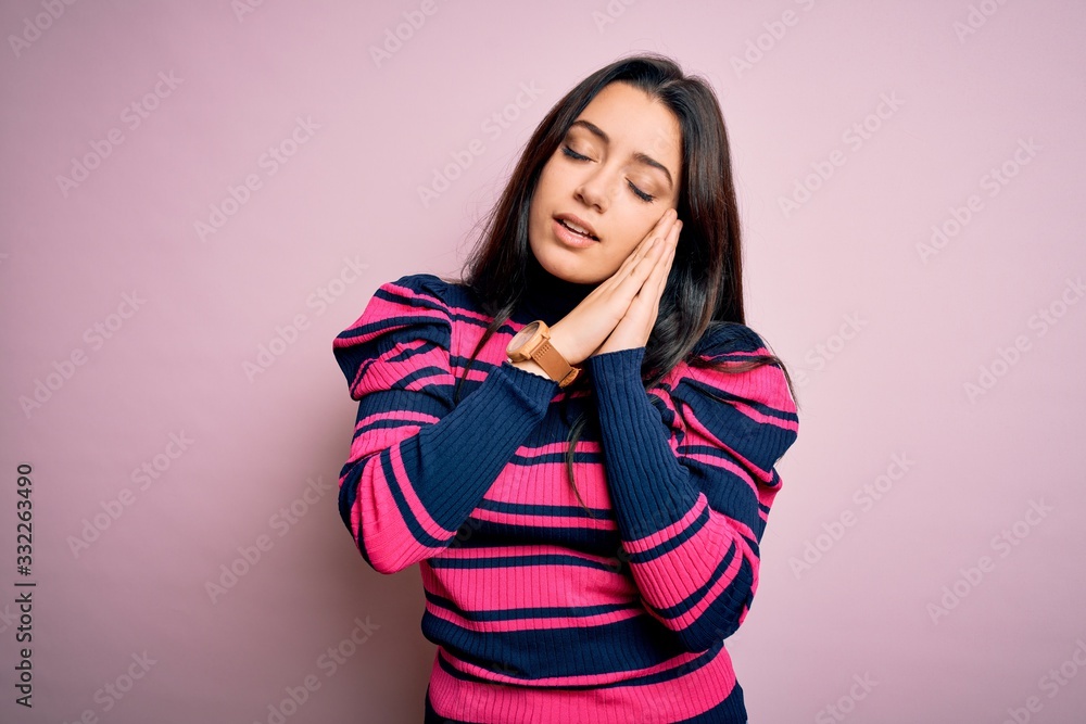 Young brunette elegant woman wearing striped shirt over pink isolated background sleeping tired dreaming and posing with hands together while smiling with closed eyes. Young brunette elegant woman wearing striped shirt over pink isolated background sleeping tired dreaming and posing with hands together while smiling with closed eyes.