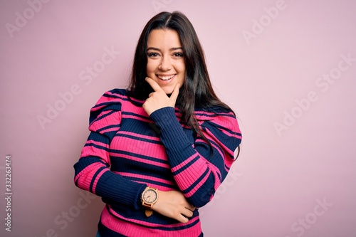 Young brunette elegant woman wearing striped shirt over pink isolated background looking confident at the camera smiling with crossed arms and hand raised on chin. Thinking positive.