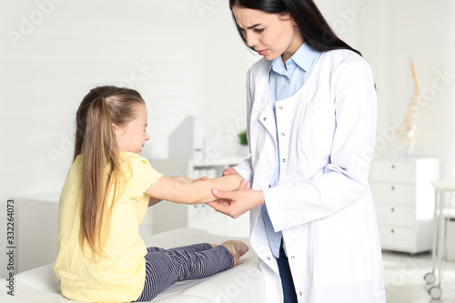 Professional orthopedist examining little patient's arm in clinic