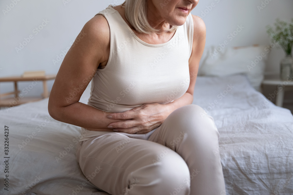Cropped image older unhealthy woman embracing belly, suffering from strong stomach ache. Unhappy middle aged lady feeling discomfort in abdomen, pancreatitis gastritis diarrhea problem concept. - obrazy, fototapety, plakaty 