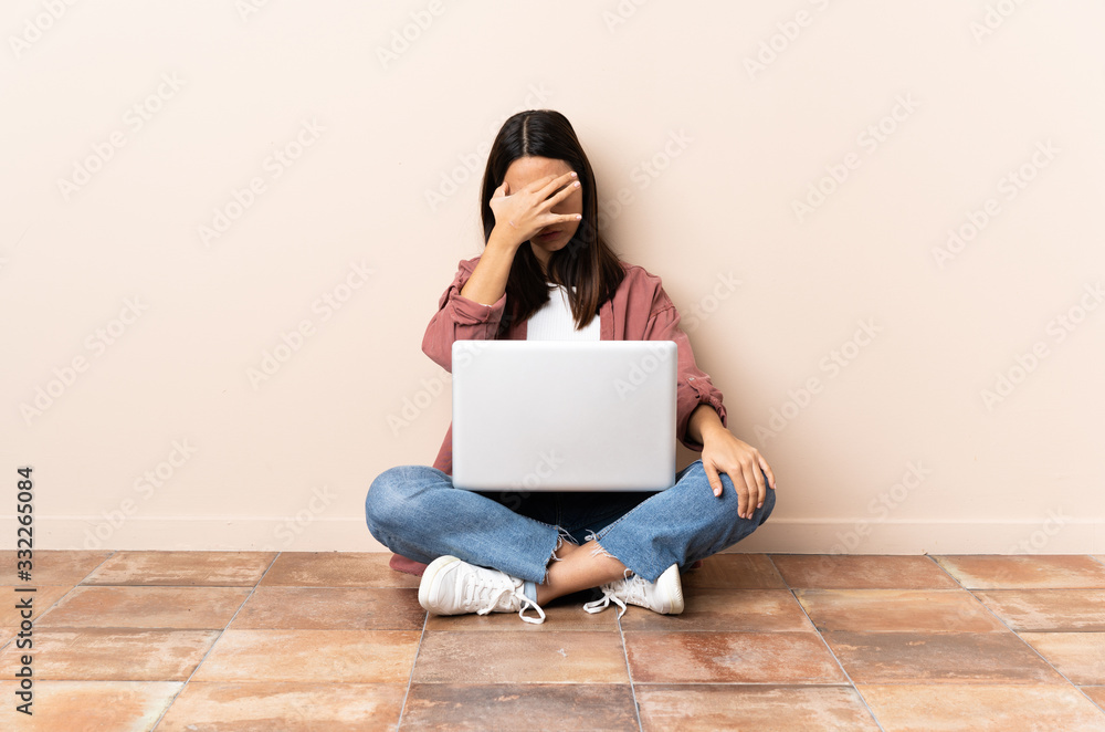 Young mixed race woman with a laptop sitting on the floor with headache Young mixed race woman with a laptop sitting on the floor with headache