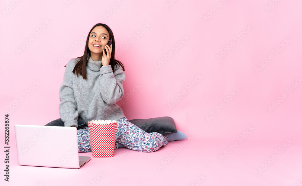 Young mixed race woman eating popcorn while watching a movie on the laptop keeping a conversation with the mobile phone Young mixed race woman eating popcorn while watching a movie on the laptop keeping a conversation with the mobile phone