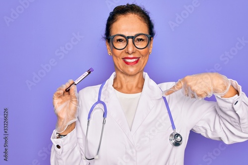 Middle age senior female doctor holding medice blood sample of coronavirus infection disease with surprise face pointing finger to himself photo