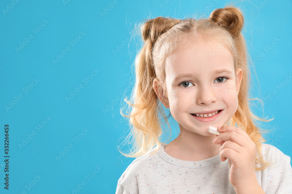 Little girl taking vitamin pill on light blue background. Space for text