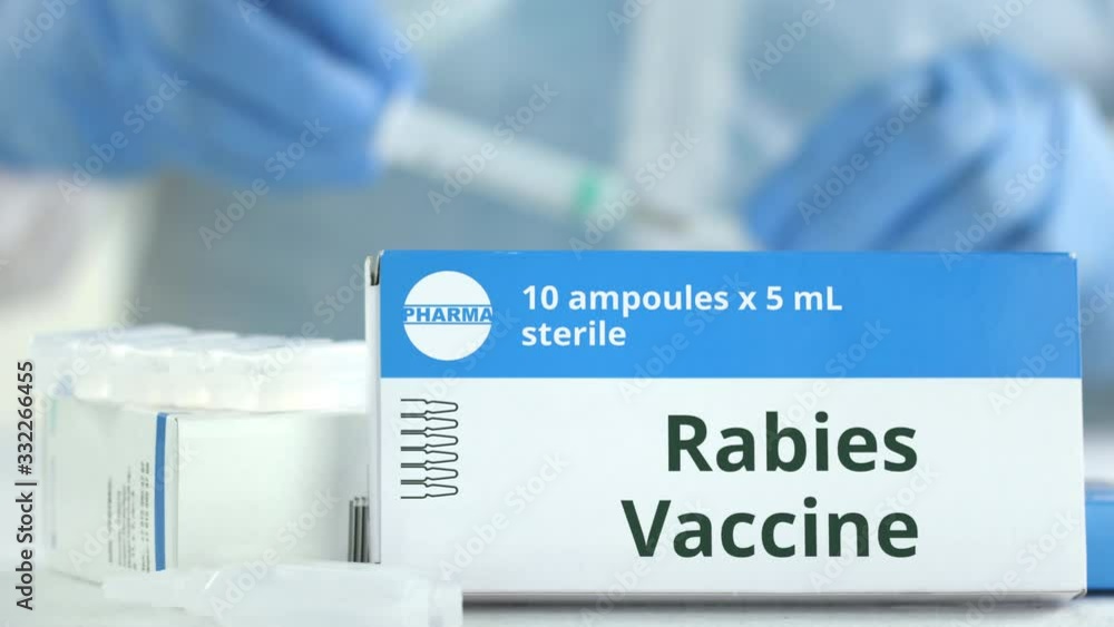 Box with rabies vaccine on the table against blurred lab assistant or doctor. Fictional phaceutical logo Box with rabies vaccine on the table against blurred lab assistant or doctor. Fictional phaceutical logo