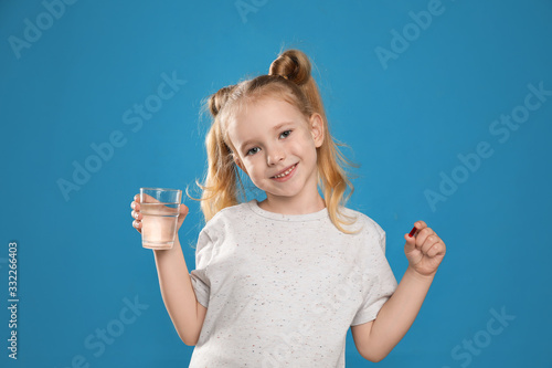 Little girl with vitamin pill and glass of water on blue background