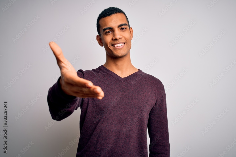 Young handsome african american man wearing casual sweater over white background smiling friendly offering handshake as greeting and welcoming. Successful business. Young handsome african american man wearing casual sweater over white background smiling friendly offering handshake as greeting and welcoming. Successful business.