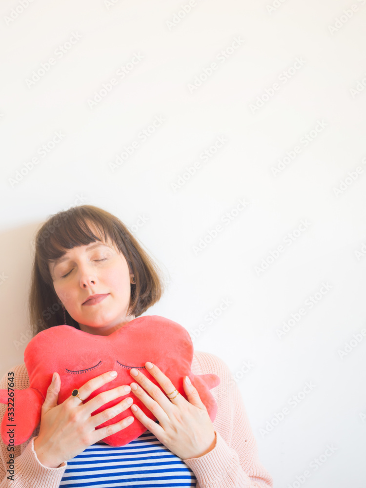 Young woman wearing striped t-shirt hugging red heart shaped plush toy Young woman wearing striped t-shirt hugging red heart shaped plush toy