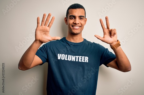 Young handsome african american man volunteering wearing t-shirt with volunteer message showing and pointing up with fingers number eight while smiling confident and happy. © Krakenimages.com