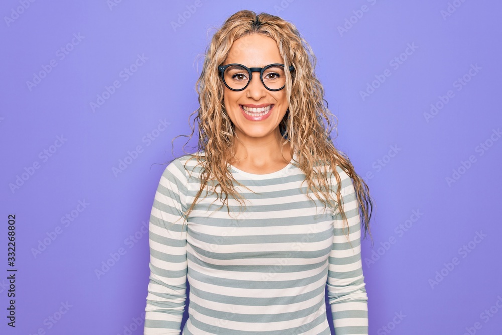 Beautiful blonde woman wearing casual striped t-shirt and glasses over purple background with a happy and cool smile on face. Lucky person. Beautiful blonde woman wearing casual striped t-shirt and glasses over purple background with a happy and cool smile on face. Lucky person.