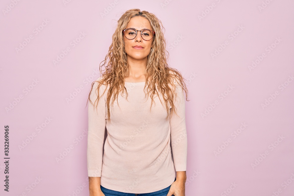 Obraz premium Young beautiful blonde woman wearing casual sweater and glasses over pink background Relaxed with serious expression on face. Simple and natural looking at the camera.