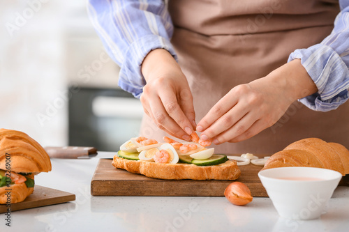 Woman preparing tasty croissant sandwich in kitchen, closeup