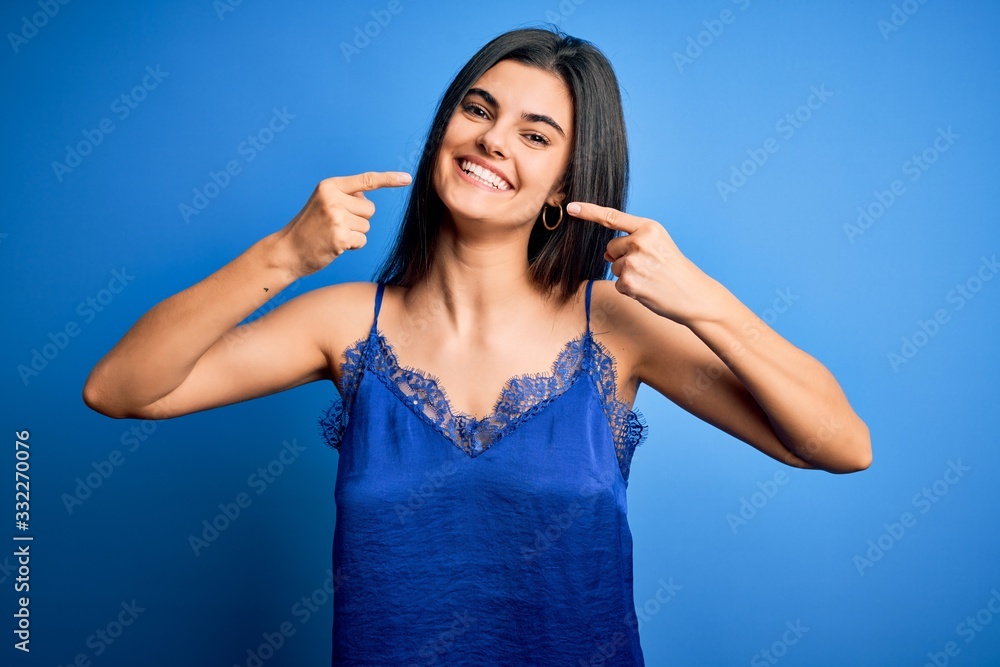 Young beautiful brunette woman wearing elegant and comfortable blue lingerie underwear smiling cheerful showing and pointing with fingers teeth and mouth. Dental health concept. Young beautiful brunette woman wearing elegant and comfortable blue lingerie underwear smiling cheerful showing and pointing with fingers teeth and mouth. Dental health concept.