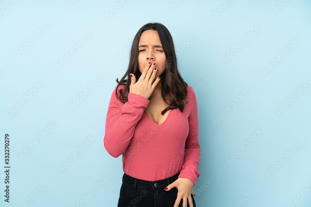 Young mixed race woman isolated on blue background yawning Young mixed race woman isolated on blue background yawning