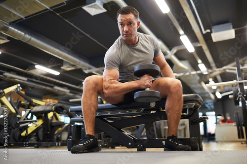Full length portrait of mature muscular man doing exercises with dumbbells during strength workout in modern gym, copy space