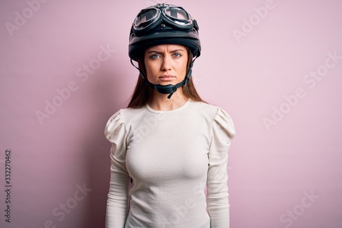 Young beautiful motorcyclist woman with blue eyes wearing moto helmet over pink background skeptic and nervous, frowning upset because of problem. Negative person.