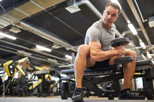 Low angle portrait of mature muscular man doing exercises with dumbbells during strength workout in modern gym, copy space