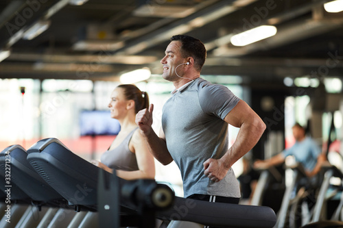 Side view portrait of mature muscular man running on treadmill while enjoying cardio workout with music in modern gym, copy space