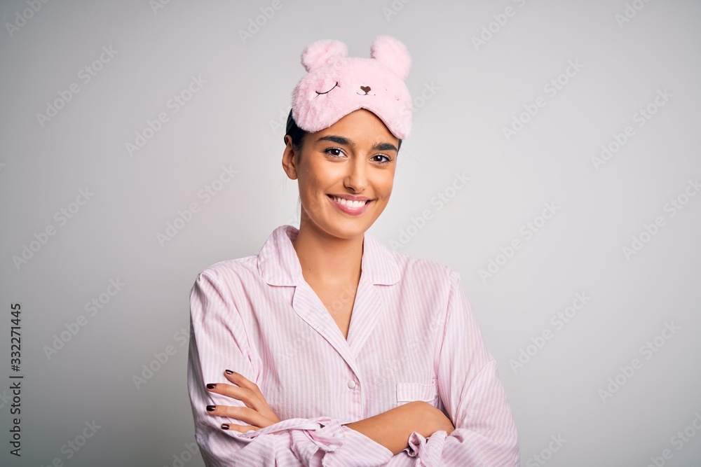 Young beautiful brunette woman wearing pajama and sleep mask over white background happy face smiling with crossed arms looking at the camera. Positive person. Young beautiful brunette woman wearing pajama and sleep mask over white background happy face smiling with crossed arms looking at the camera. Positive person.
