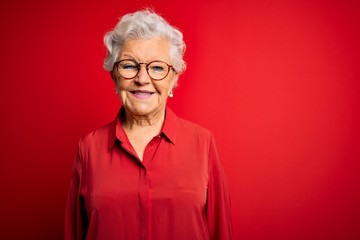 Senior beautiful grey-haired woman wearing casual shirt and glasses over red background with a happy and cool smile on face. Lucky person.