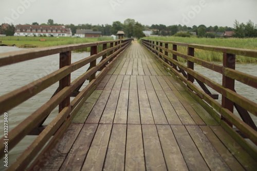 long wooden pedestrian bridge with railings across the river. background of village  srlective focus